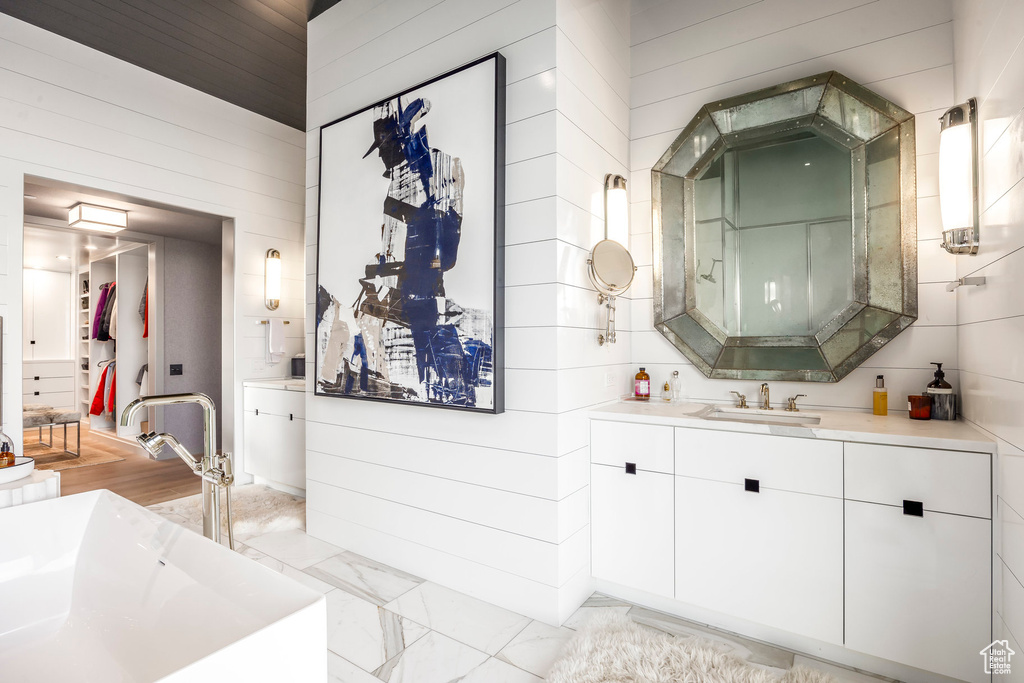 Full bath featuring a soaking tub, vanity, wood walls, and marble finish floors