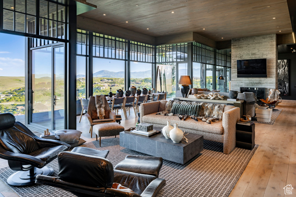 Living area with wooden ceiling, hardwood / wood-style flooring, a stone fireplace, a towering ceiling, and recessed lighting