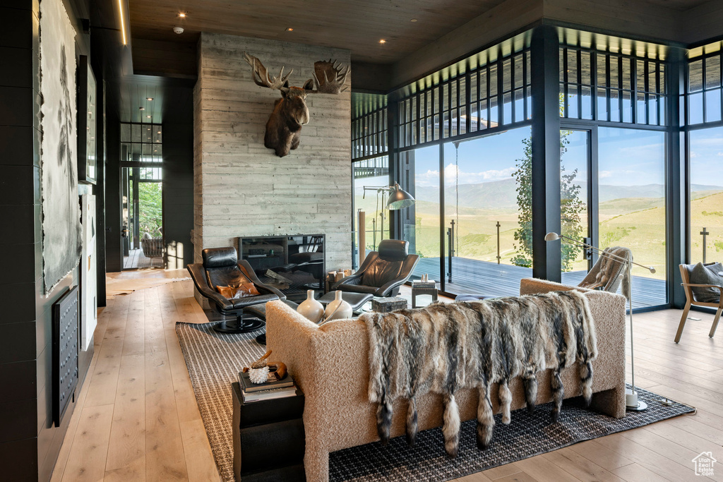 Living area with wood-type flooring, a stone fireplace, a towering ceiling, a mountain view, and expansive windows