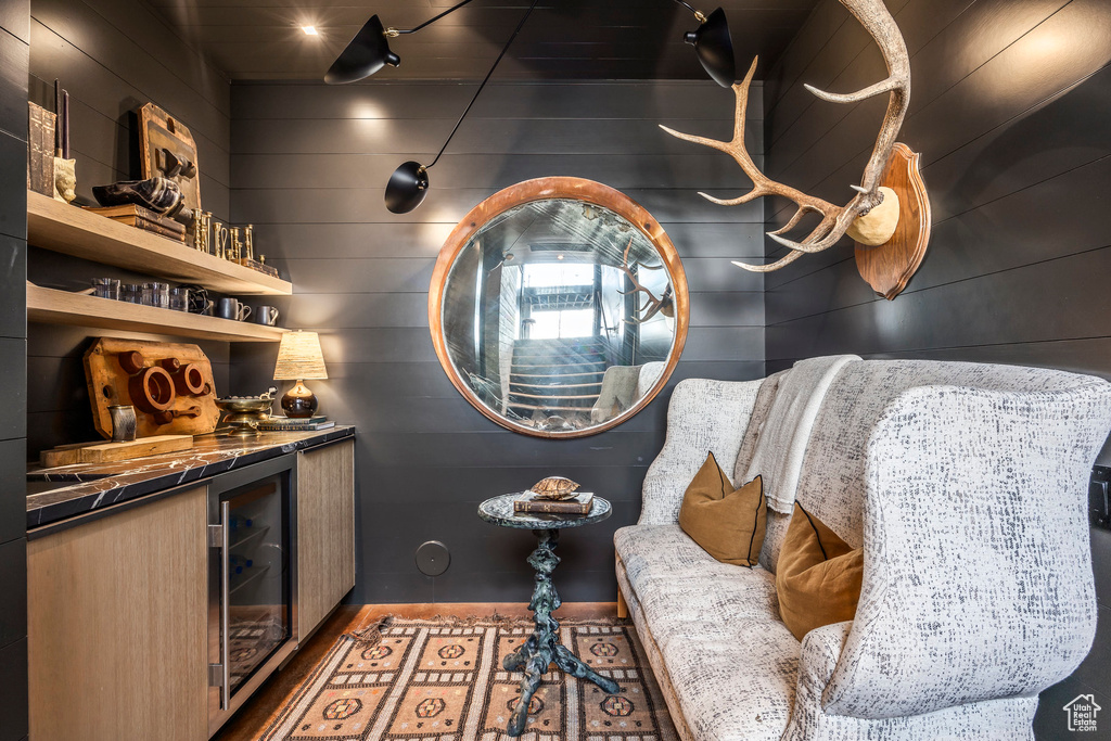 Wine area with wine cooler, a bar, wood finished floors, and wood walls