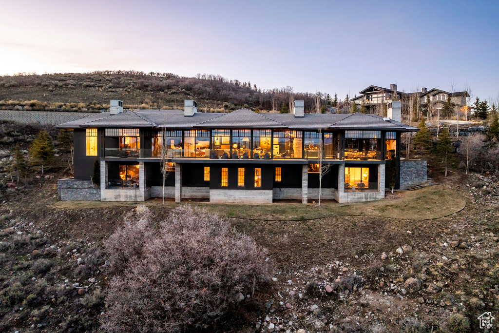 Back of property at dusk featuring a chimney, a patio, and a balcony