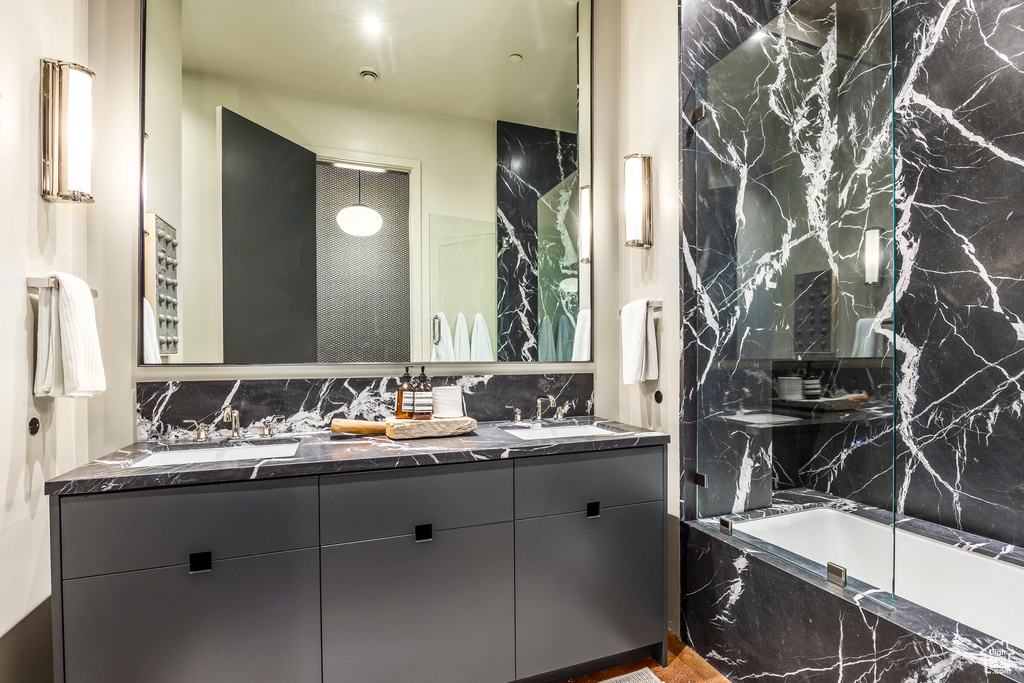 Bathroom with a tub with marble appearance, tasteful backsplash, double vanity, and a marble finish shower