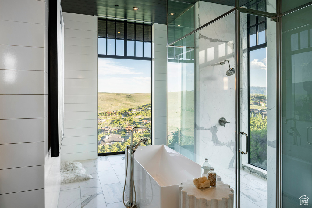 Full bathroom featuring healthy amount of natural light, a freestanding bath, marble tiled flooring, and expansive windows
