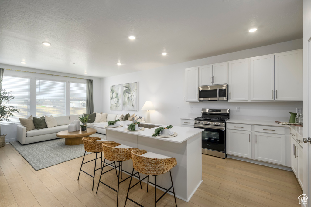 Kitchen featuring open floor plan, stainless steel appliances, a kitchen island, a sink, and light wood-style floors