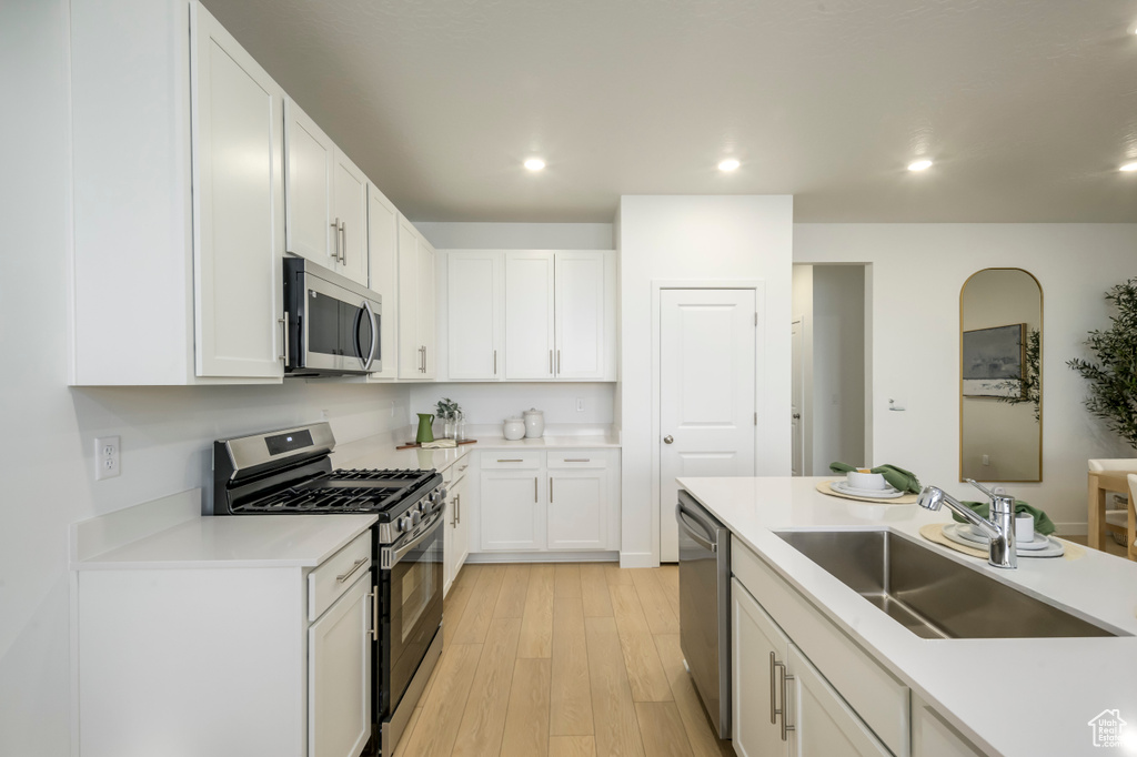 Kitchen with light wood finished floors, white cabinetry, a sink, and stainless steel appliances