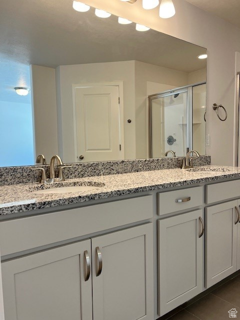 Bathroom featuring a stall shower, tile patterned floors, double vanity, and a sink