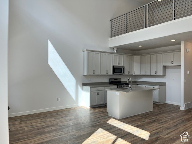 Kitchen with a center island with sink, dark wood-type flooring, baseboards, a towering ceiling, and appliances with stainless steel finishes
