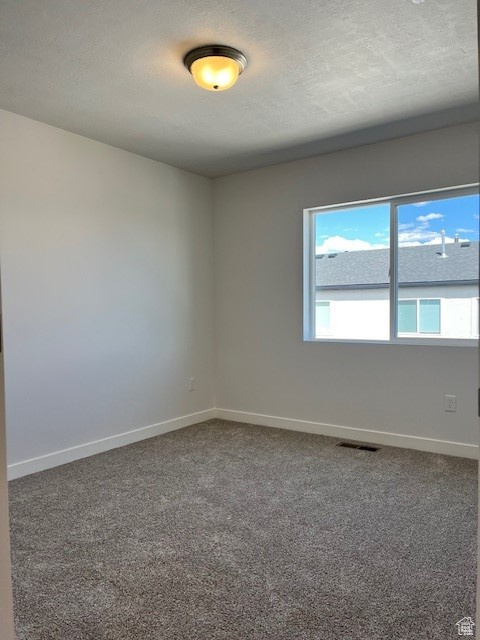 Empty room featuring a textured ceiling, carpet, baseboards, and visible vents