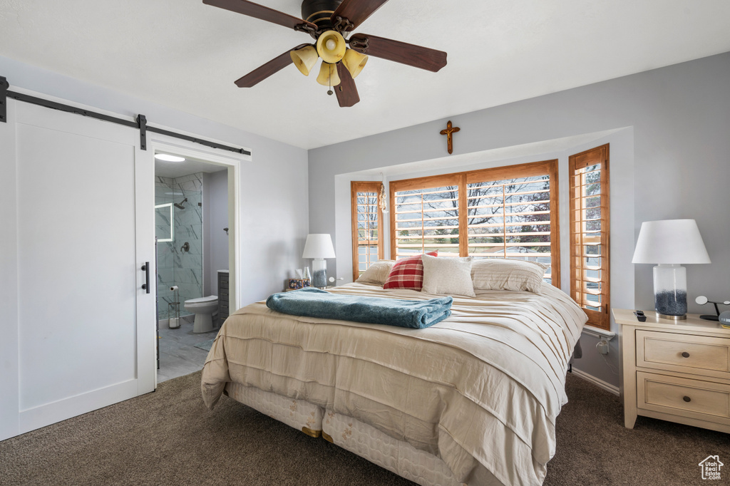 Carpeted bedroom featuring a barn door, connected bathroom, baseboards, and ceiling fan