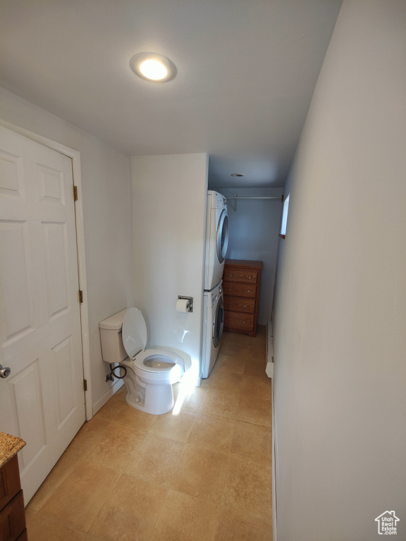 Bathroom with toilet, baseboards, and stacked washer and clothes dryer