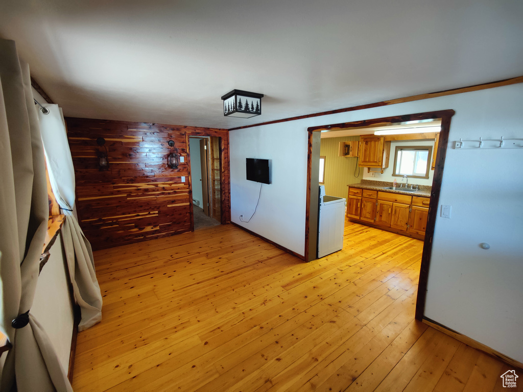 Kitchen with brown cabinetry, dark countertops, wood walls, light wood-type flooring, and a sink
