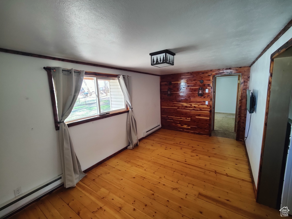 Spare room with wooden walls, baseboards, baseboard heating, and light wood finished floors