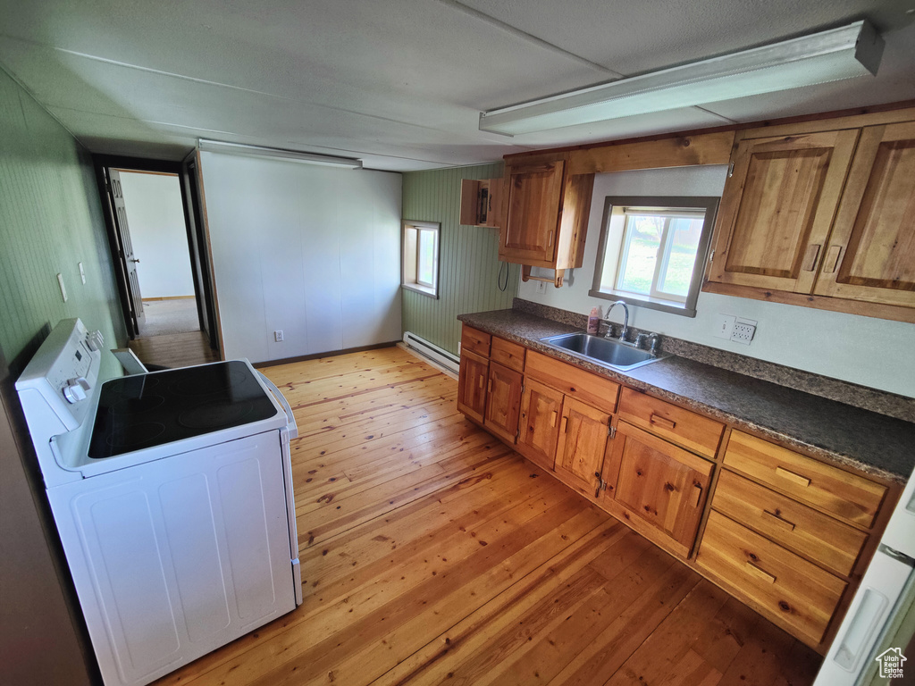 Kitchen featuring a sink, dark countertops, a baseboard heating unit, and light wood-style flooring