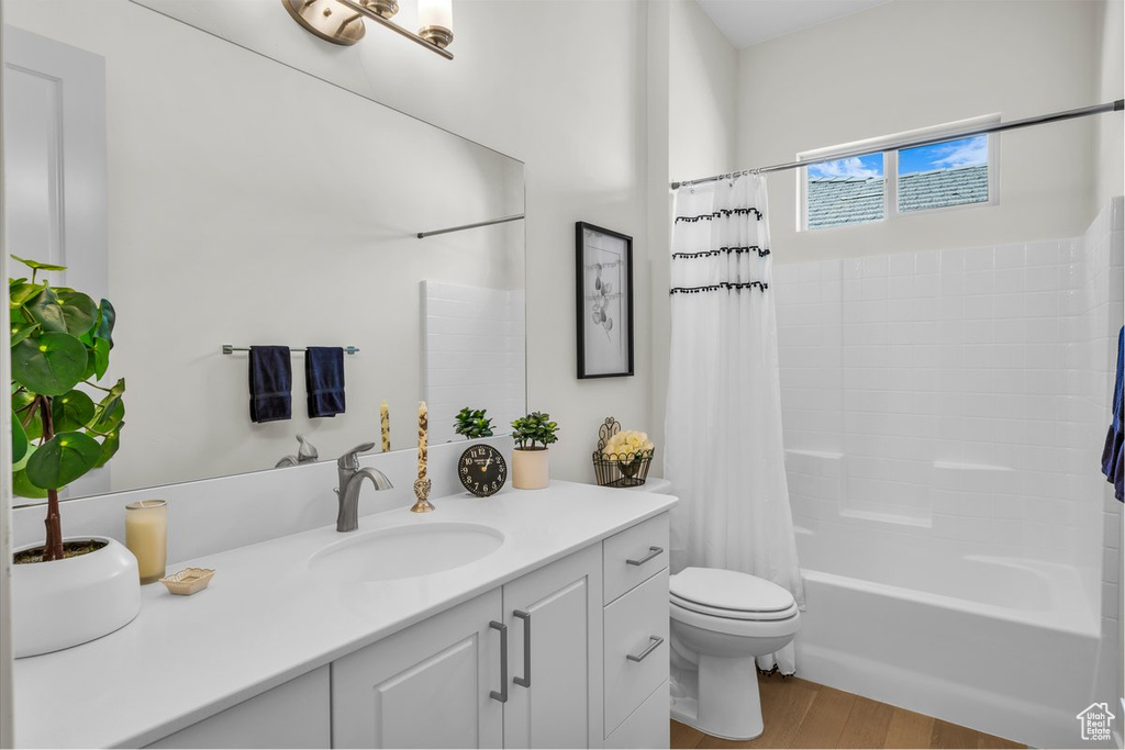Bathroom with wood finished floors, toilet, shower / tub combo with curtain, and vanity