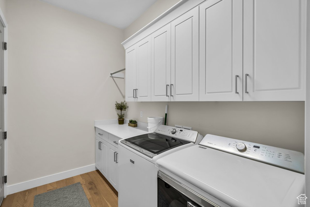 Laundry area with baseboards, washing machine and dryer, cabinet space, and light wood-type flooring