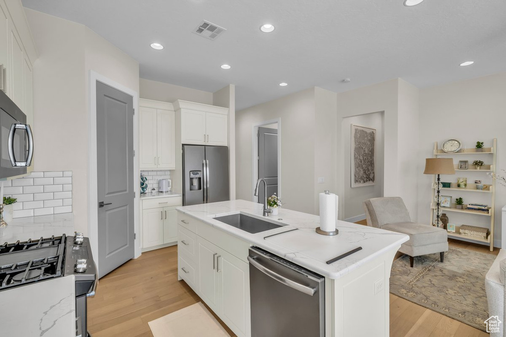 Kitchen featuring white cabinets, visible vents, light wood finished floors, stainless steel appliances, and a sink