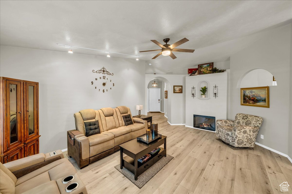 Living area featuring a glass covered fireplace, light wood-type flooring, baseboards, arched walkways, and ceiling fan