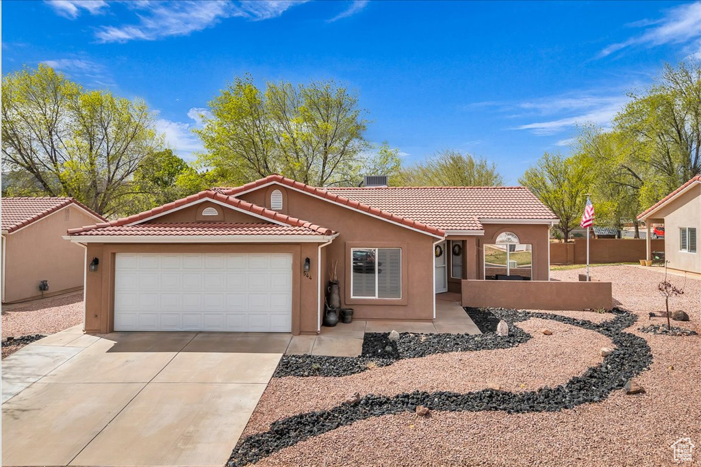 View of front of home featuring a tile roof, stucco siding, fence, driveway, and a garage