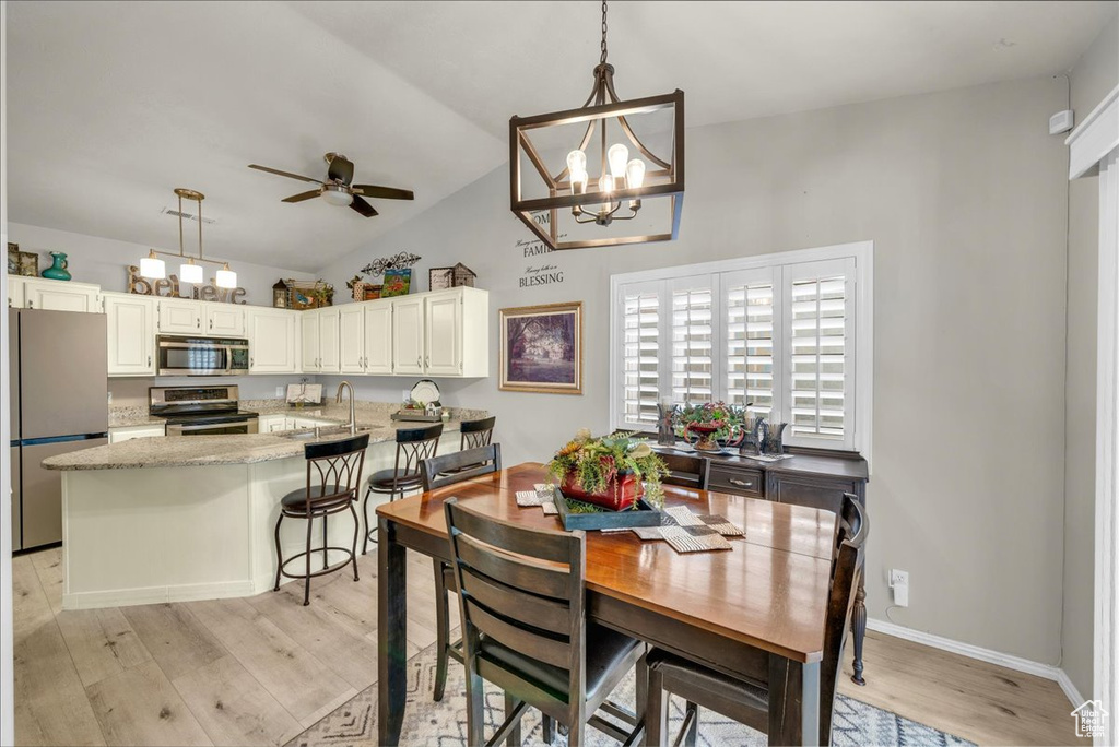 Dining space with baseboards, vaulted ceiling, ceiling fan with notable chandelier, and light wood finished floors