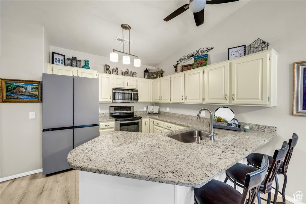 Kitchen with stainless steel appliances, a sink, light stone counters, ceiling fan, and a peninsula