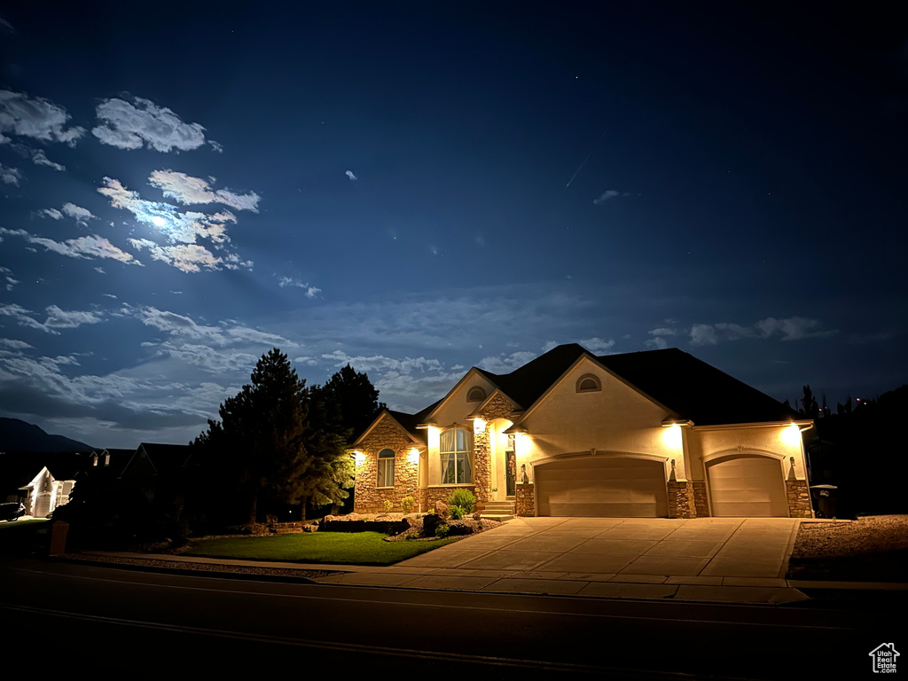 French provincial home with stone siding, an attached garage, stucco siding, concrete driveway, and a yard