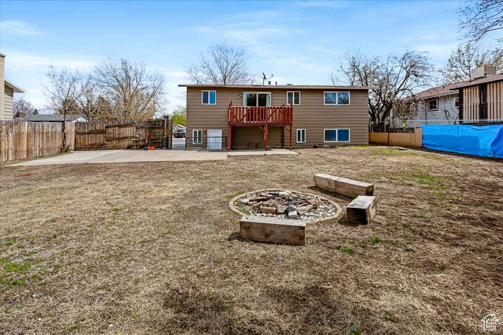 Back of house with a fire pit, a deck, a fenced backyard, a patio, and a lawn