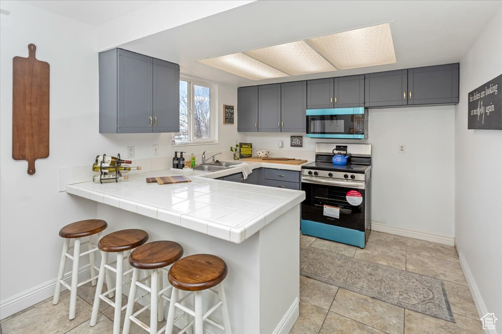 Kitchen with a peninsula, appliances with stainless steel finishes, a sink, gray cabinets, and a kitchen breakfast bar
