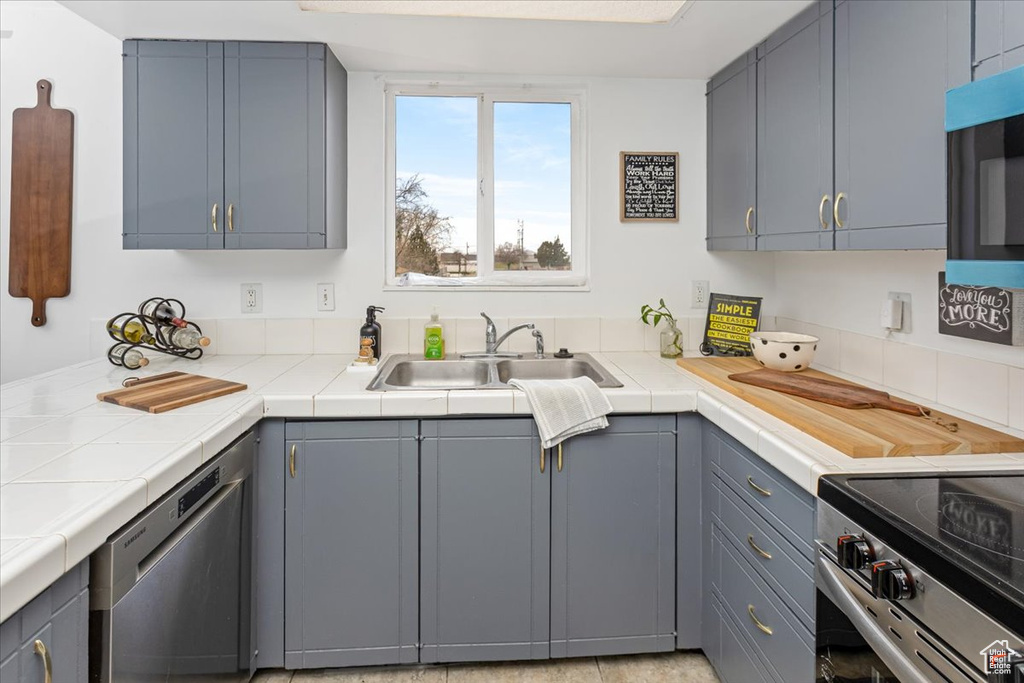 Kitchen featuring tile counters, a sink, gray cabinets, and appliances with stainless steel finishes