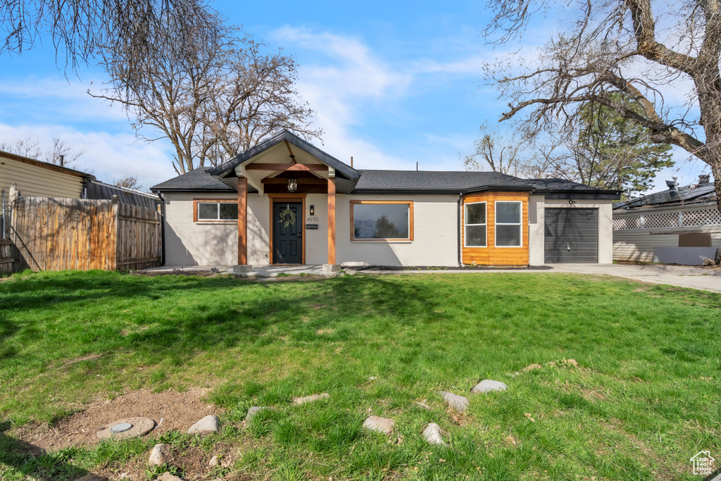 View of front facade featuring a front lawn, driveway, fence, and a garage