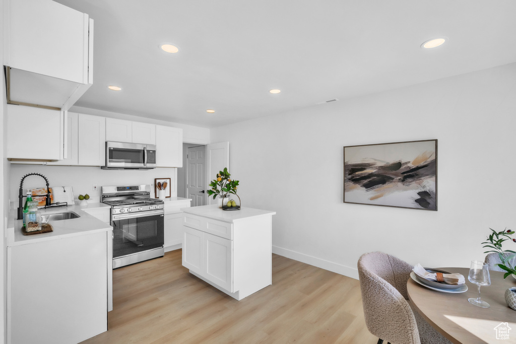 Kitchen featuring light countertops, light wood-style flooring, appliances with stainless steel finishes, white cabinetry, and a sink