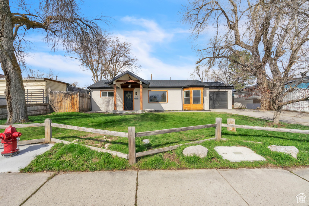 Mid-century home with driveway, an attached garage, a fenced front yard, and a front yard