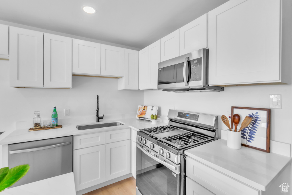 Kitchen with light countertops, a sink, white cabinetry, appliances with stainless steel finishes, and light wood-style floors