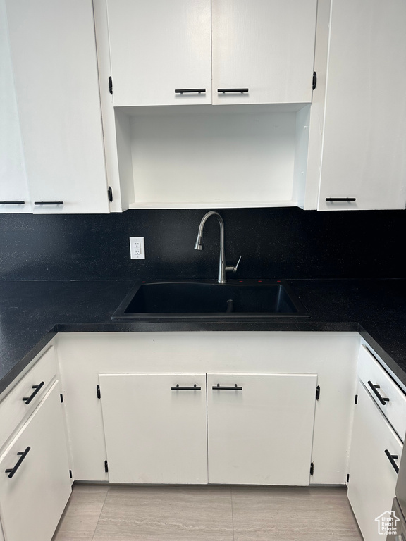 Kitchen with white cabinetry, tasteful backsplash, dark countertops, and a sink