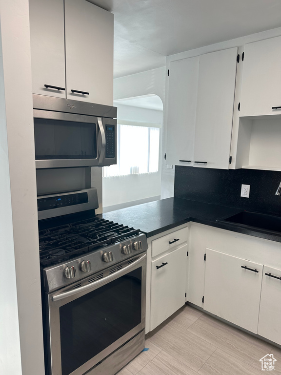 Kitchen featuring white cabinetry, dark countertops, a sink, and stainless steel appliances