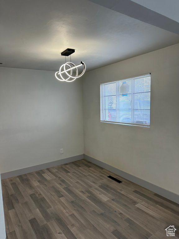 Unfurnished room featuring wood finished floors, baseboards, a chandelier, and visible vents