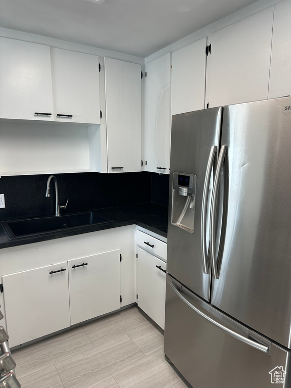 Kitchen featuring white cabinetry, dark countertops, stainless steel fridge, and a sink