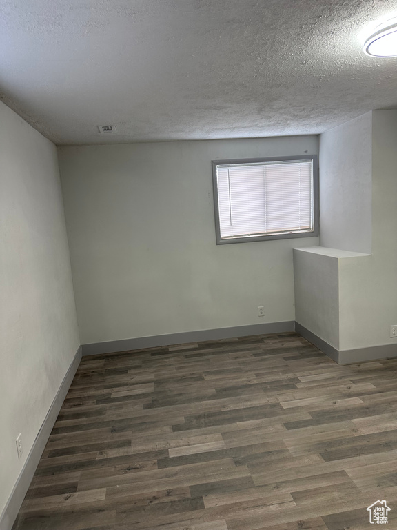 Empty room with visible vents, a textured ceiling, baseboards, and wood finished floors