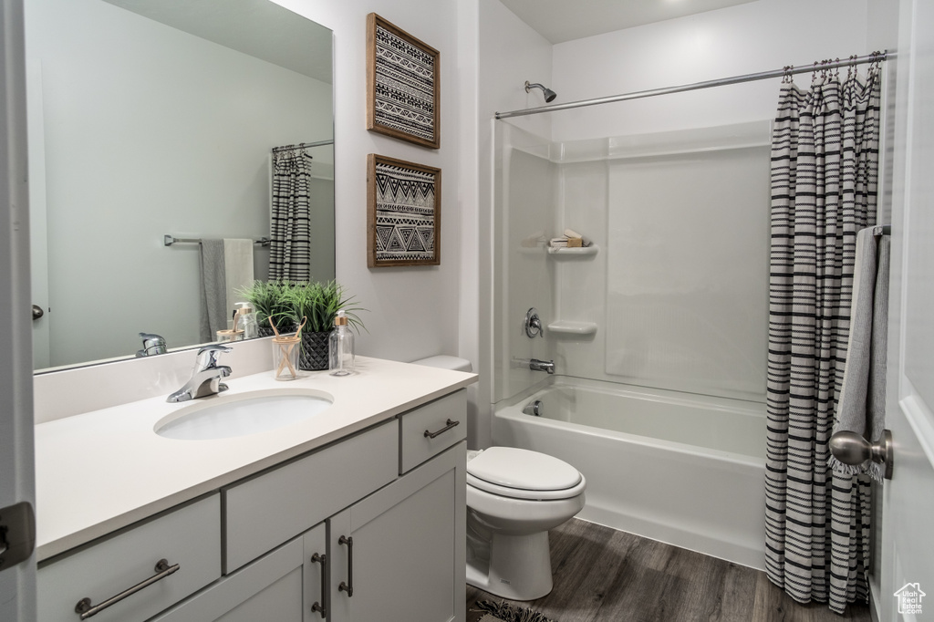 Full bath with shower / tub combo with curtain, wood finished floors, toilet, and vanity