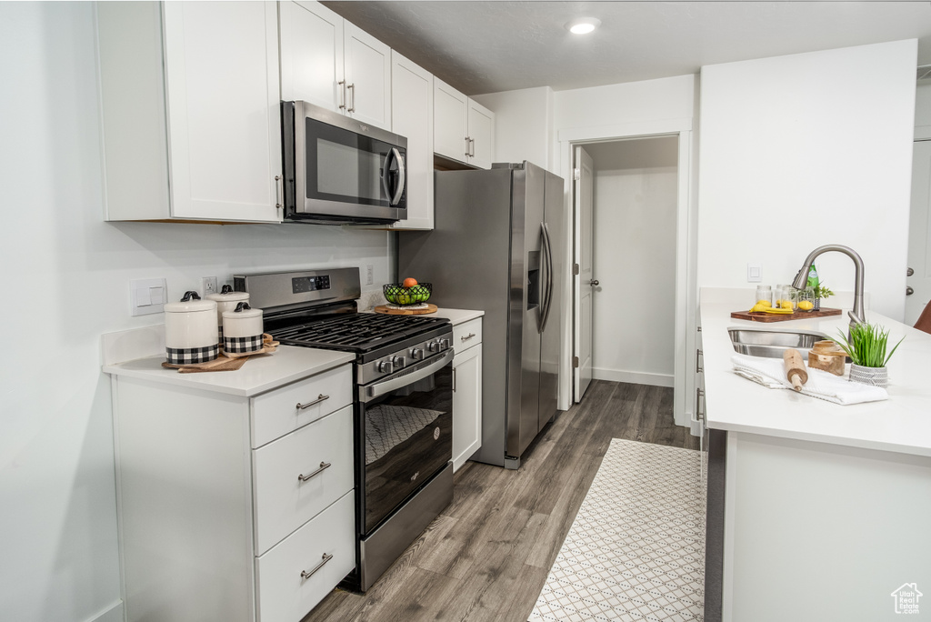 Kitchen featuring light countertops, a sink, white cabinetry, wood finished floors, and appliances with stainless steel finishes