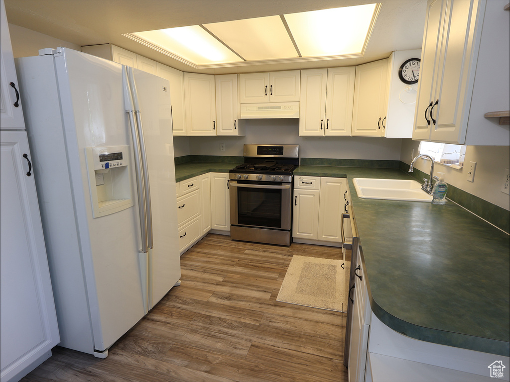 Kitchen with wood finished floors, dark countertops, white refrigerator with ice dispenser, stainless steel range with gas stovetop, and a sink