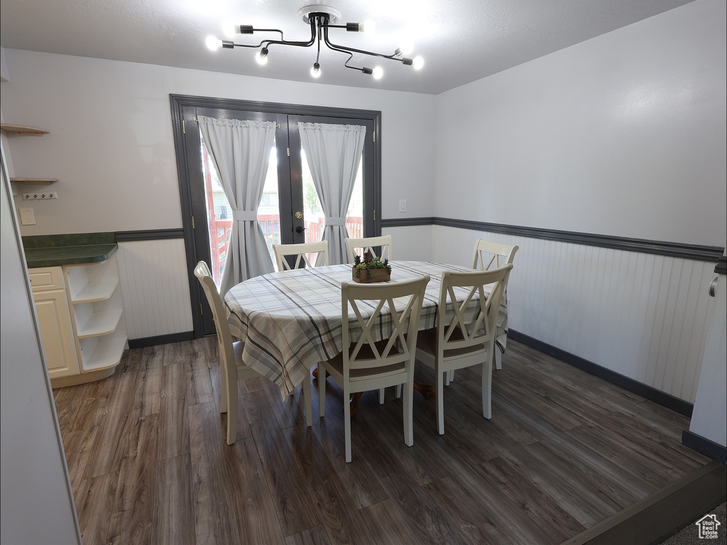 Dining area featuring a wainscoted wall, french doors, dark wood-style floors, and a notable chandelier