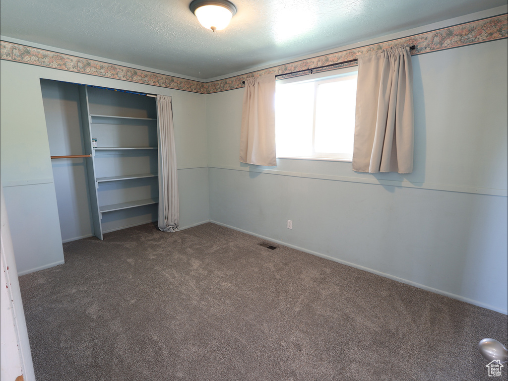 Unfurnished bedroom with carpet flooring, baseboards, visible vents, and a closet