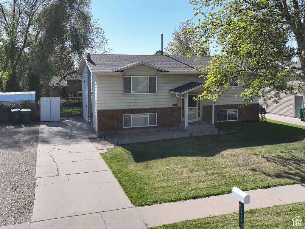 Bi-level home featuring brick siding, a front lawn, roof with shingles, and fence