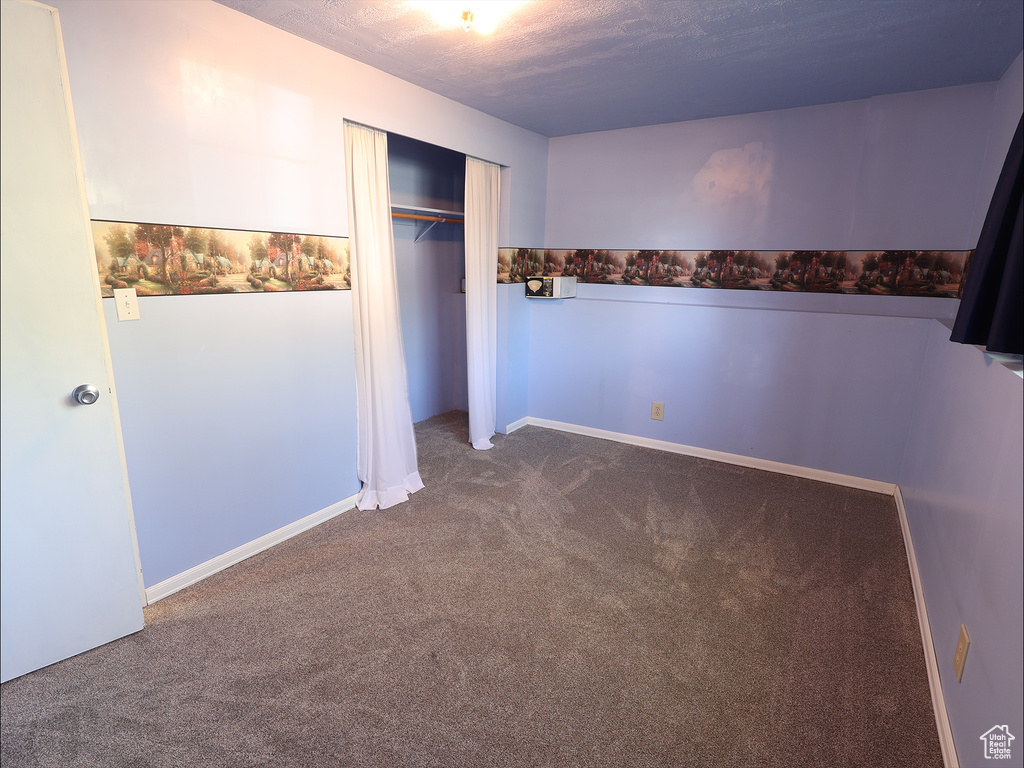 Unfurnished bedroom featuring a closet, baseboards, a textured ceiling, and dark colored carpet