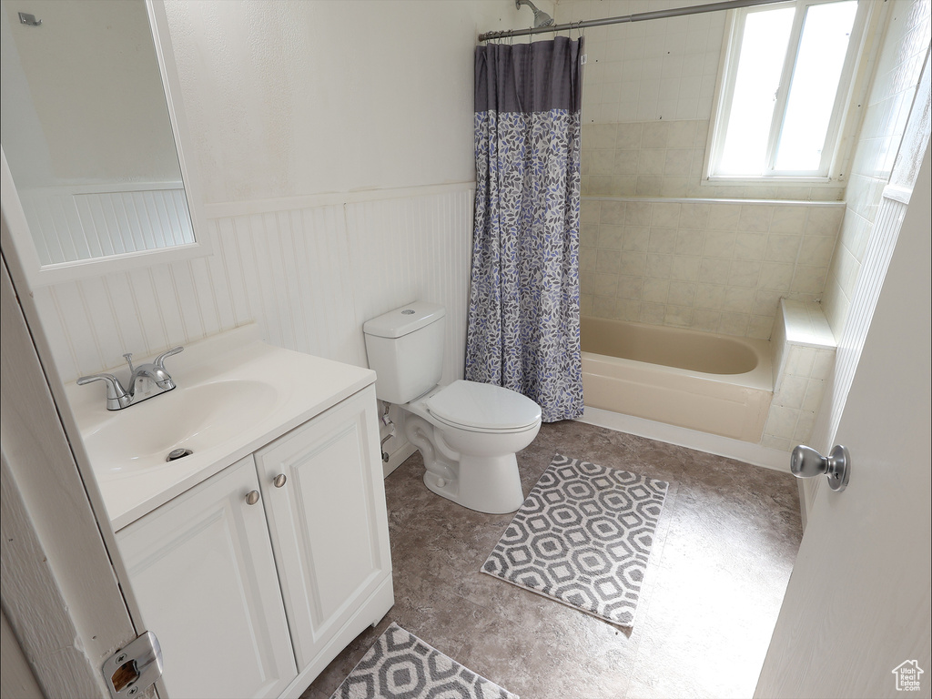 Bathroom featuring vanity, shower / tub combo with curtain, wainscoting, and toilet