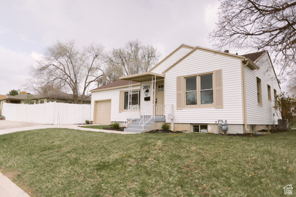 View of front of home featuring driveway, a front lawn, fence, and an attached garage