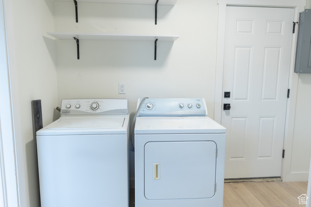 Washroom with electric panel, light wood finished floors, washing machine and clothes dryer, and laundry area
