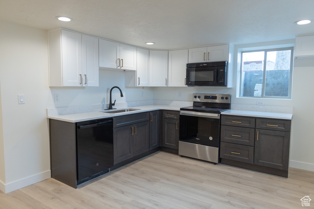Kitchen with a sink, white cabinetry, black appliances, and light countertops
