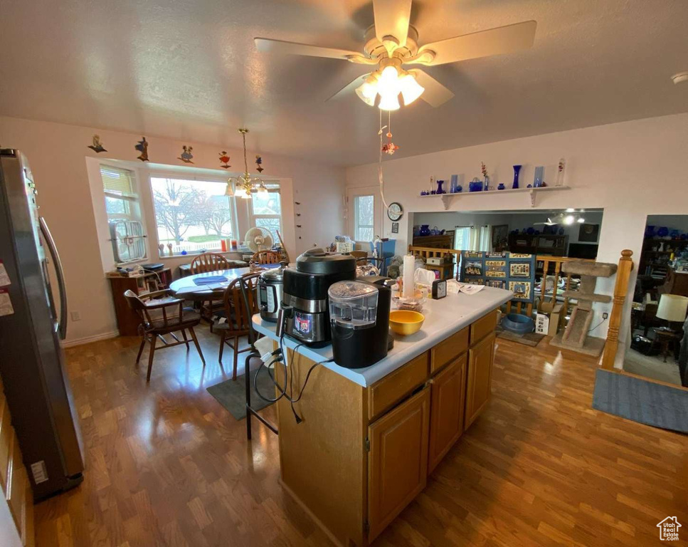 Kitchen with light countertops, wood finished floors, ceiling fan with notable chandelier, a center island, and freestanding refrigerator