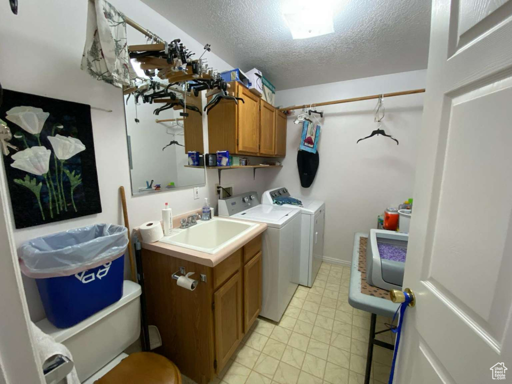 Laundry area featuring baseboards, a textured ceiling, a sink, cabinet space, and washer and dryer